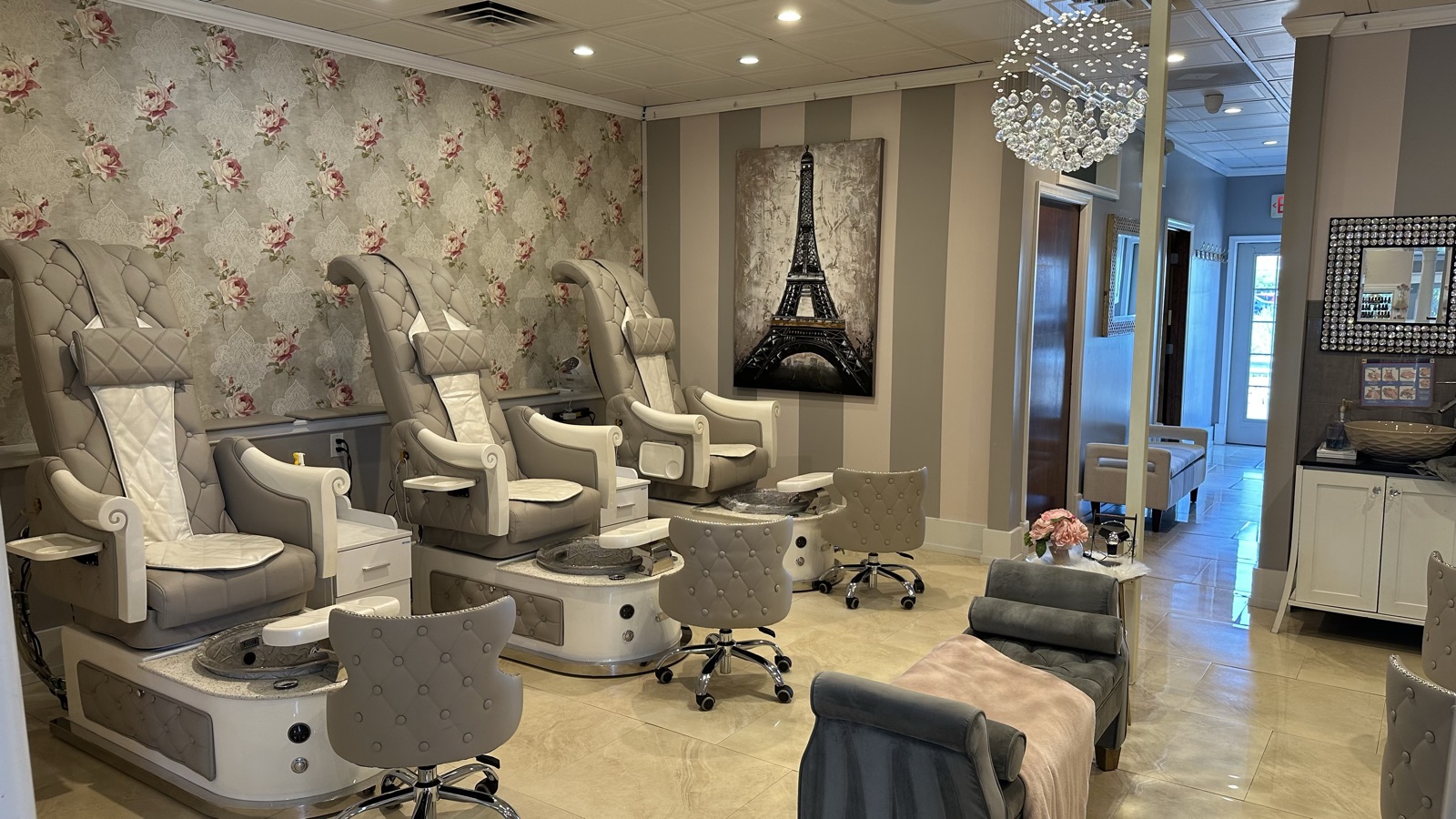 Main pedicure room with three white tufted thrones and crystal chandelier